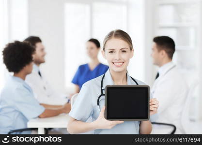 clinic, profession, people and medicine concept - happy female doctor showing tablet pc computer blank screen over group of medics meeting at hospital