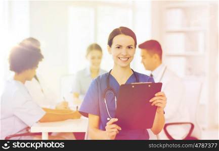 clinic, profession, people and medicine concept - happy female doctor with clipboard over group of medics meeting at hospital