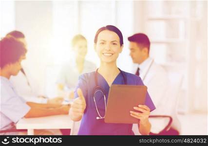 clinic, profession, people and medicine concept - happy female doctor with tablet pc computer over group of medics meeting at hospital showing thumbs up gesture