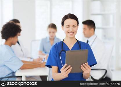 clinic, profession, people and medicine concept - happy female doctor with tablet pc computer over group of medics meeting at hospital