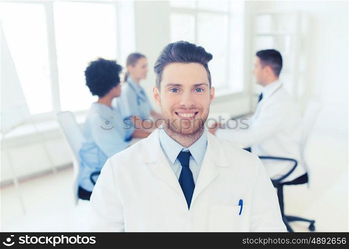 clinic, profession, people and medicine concept - happy male doctor over group of medics meeting at hospital