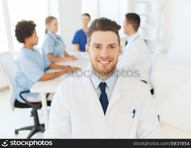 clinic, profession, people and medicine concept - happy male doctor over group of medics meeting at hospital