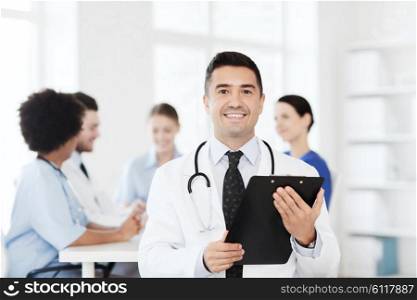 clinic, profession, people and medicine concept - happy male doctor with clipboard over group of medics meeting at hospital