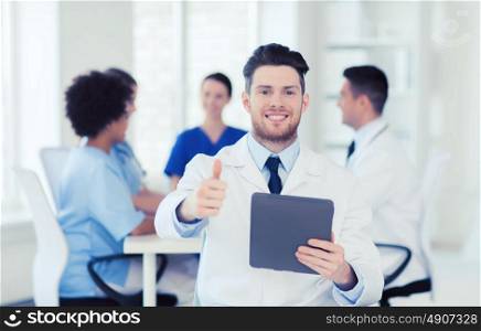 clinic, profession, people and medicine concept - happy male doctor with tablet pc computer over group of medics meeting at hospital showing thumbs up gesture. happy doctor with tablet pc over team at clinic