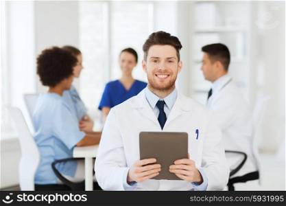 clinic, profession, people and medicine concept - happy male doctor with tablet pc computer over group of medics meeting at hospital