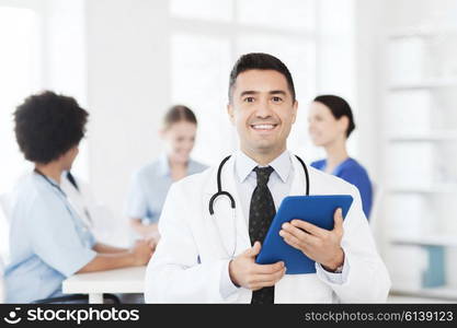 clinic, profession, people and medicine concept - happy male doctor with tablet pc computer over group of medics meeting at hospital