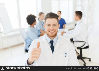 clinic, profession, people, gesture and medicine concept - happy male doctor over group of medics meeting at hospital showing thumbs up gesture