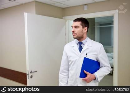 clinic, profession, people, health care and medicine concept - doctor with clipboard at hospital corridor