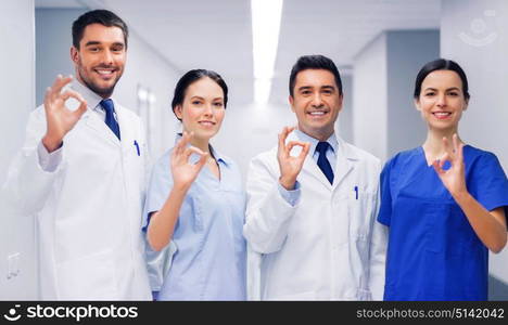 clinic, profession, people, health care and medicine concept - group of happy medics or doctors at hospital corridor showing ok hand sign. group of medics at hospital showing ok hand sign