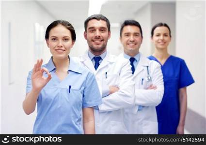 clinic, profession, people, health care and medicine concept - group of happy medics or doctors at hospital corridor showing ok hand sign. group of happy medics or doctors at hospital