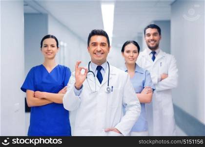 clinic, profession, people, health care and medicine concept - group of happy medics or doctors at hospital corridor showing ok hand sign. group of medics at hospital showing ok hand sign
