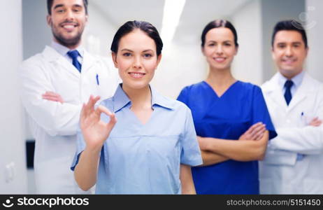 clinic, profession, people, health care and medicine concept - group of happy medics or doctors at hospital corridor showing ok hand sign. group of medics at hospital showing ok hand sign