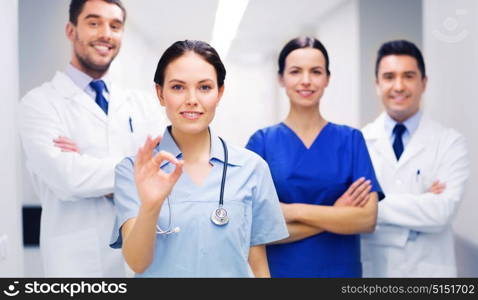 clinic, profession, people, health care and medicine concept - group of happy medics or doctors at hospital corridor showing ok hand sign. group of medics at hospital showing ok hand sign