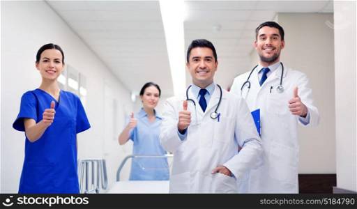 clinic, profession, people, health care and medicine concept - group of happy medics or doctors with gurney showing thumbs up at hospital corridor. happy doctors showing thumbs up at hospital