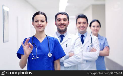 clinic, profession, people, health care and medicine concept - group of happy medics or doctors at hospital corridor showing ok hand sign. group of happy medics or doctors at hospital