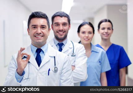 clinic, profession, people, health care and medicine concept - group of happy medics or doctors at hospital corridor showing ok hand sign. group of happy medics or doctors at hospital