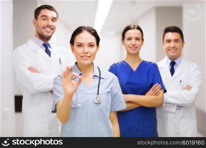 clinic, profession, people, health care and medicine concept - group of happy medics or doctors at hospital corridor showing ok hand sign