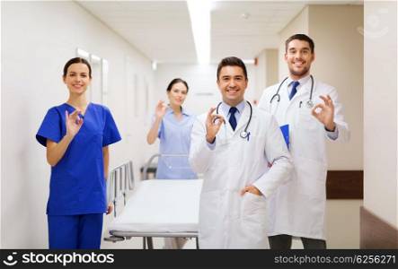 clinic, profession, people, health care and medicine concept - group of happy medics or doctors with gurney showing ok hand sign at hospital corridor
