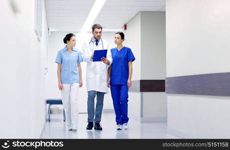 clinic, profession, people, health care and medicine concept - group of medics or doctors with clipboard walking along hospital corridor. group of medics at hospital with clipboard