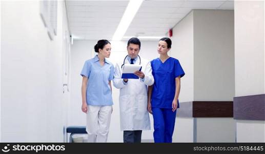 clinic, profession, people, health care and medicine concept - group of medics or doctors with clipboard walking along hospital corridor. group of medics at hospital with clipboard