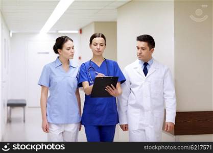 clinic, profession, people, health care and medicine concept - group of medics or doctors with clipboard walking along hospital corridor