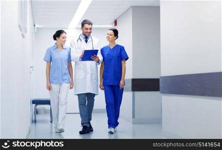 clinic, profession, people, health care and medicine concept - group of smiling medics or doctors with clipboard walking along hospital corridor. group of medics at hospital with clipboard