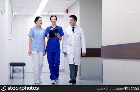 clinic, profession, people, health care and medicine concept - group of smiling medics or doctors with clipboard walking along hospital corridor. group of smiling medics at hospital with clipboard