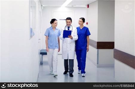 clinic, profession, people, health care and medicine concept - group of smiling medics or doctors with clipboard walking along hospital corridor. group of smiling medics at hospital with clipboard