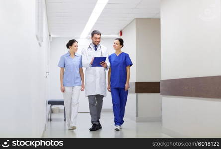 clinic, profession, people, health care and medicine concept - group of smiling medics or doctors with clipboard walking along hospital corridor