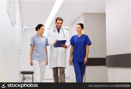 clinic, profession, people, health care and medicine concept - group of smiling medics or doctors with clipboard walking along hospital corridor