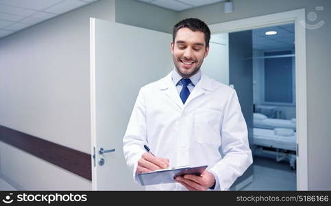 clinic, profession, people, health care and medicine concept - smiling doctor with clipboard at hospital corridor. smiling doctor with clipboard at hospital