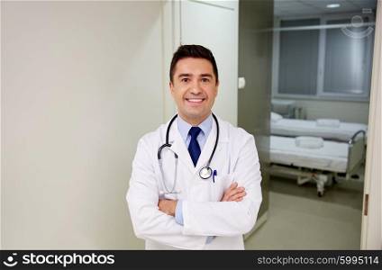 clinic, profession, people, health care and medicine concept - smiling doctor with stethoscope at hospital corridor