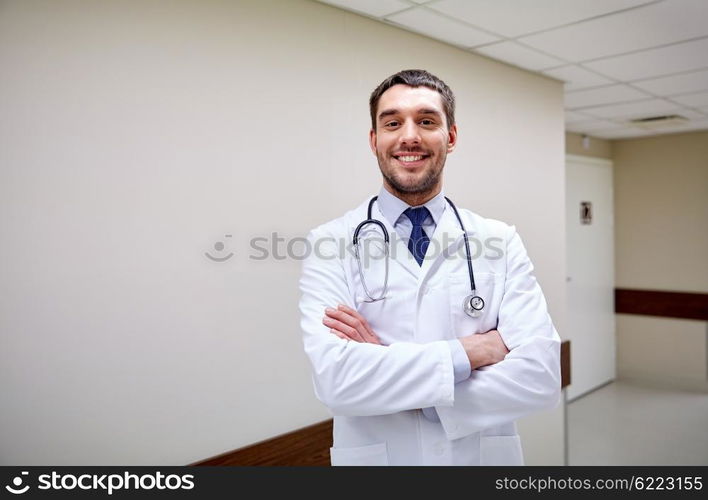 clinic, profession, people, health care and medicine concept - smiling doctor with stethoscope at hospital corridor