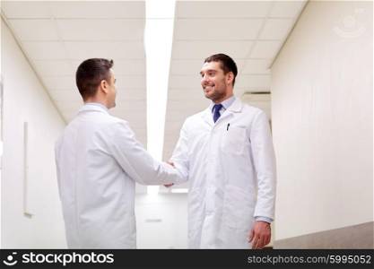 clinic, profession, people, health care and medicine concept - smiling doctors meeting and greeting by handshake at hospital corridor