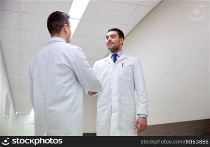 clinic, profession, people, health care and medicine concept - smiling doctors meeting and greeting by handshake at hospital corridor