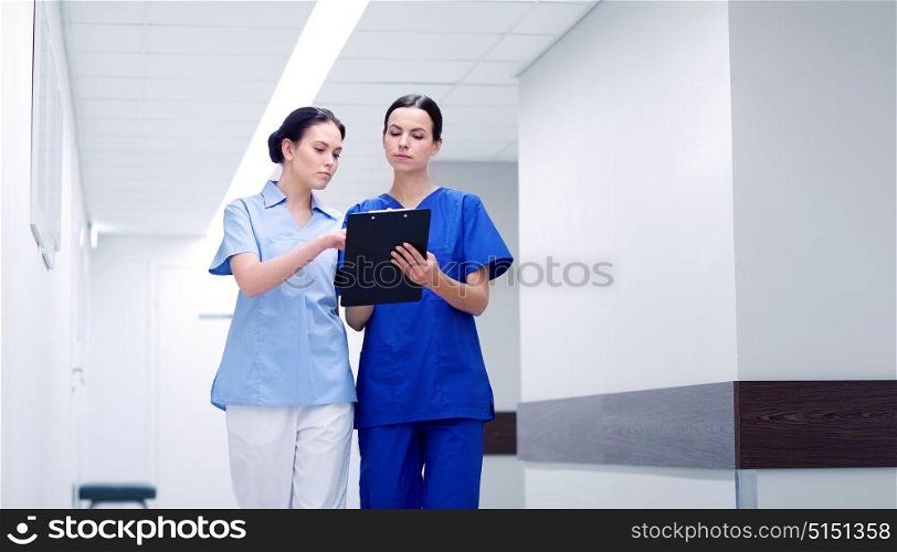 clinic, profession, people, health care and medicine concept - two medics or nurses with clipboard walking along hospital corridor. two medics or nurses at hospital with clipboard
