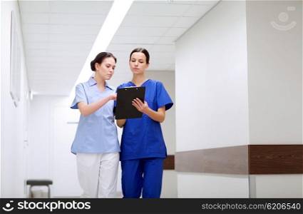 clinic, profession, people, health care and medicine concept - two medics or nurses with clipboard walking along hospital corridor