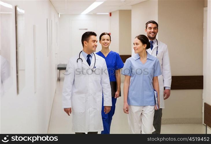 clinic, profession, people, healthcare and medicine concept - group of happy medics or doctors walking along hospital corridor