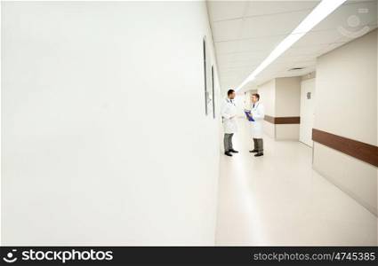 clinic, profession, people, healthcare and medicine concept - male doctors talking at hospital corridor