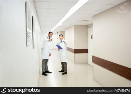 clinic, profession, people, healthcare and medicine concept - male doctors with clipboard pointing finger to something at hospital