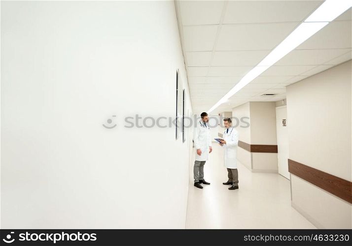 clinic, profession, people, healthcare and medicine concept - male doctors with clipboard at hospital corridor
