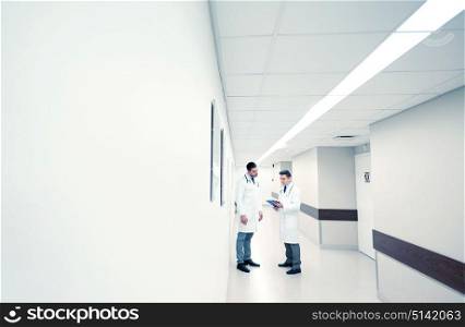 clinic, profession, people, healthcare and medicine concept - male doctors with clipboard at hospital corridor. male doctors with clipboard at hospital corridor