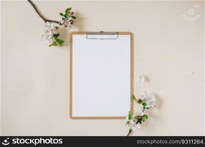 Clipboard tablet pad with blank copy space and white apple flowers on beige backdrop. Flat lay, top view template. Female office desk