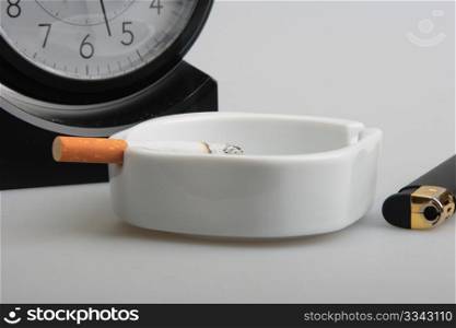 Clock and white ashtray with cigarette. Studio photography. Close-up.