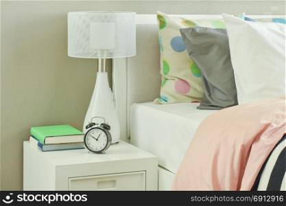 Clock and white table lamp next to striped bedding