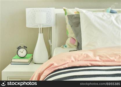 Clock and white table lamp next to striped bedding