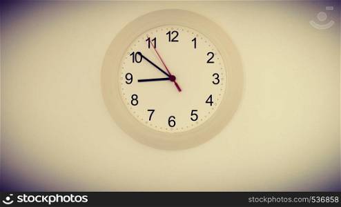 Clock hanging on white wall showing nine hours. Toned image with vignette. clock on wall showing nine hours