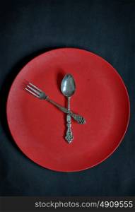 Clock with red plate, spoon and fork on rusty background