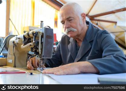 close-aged man repairs fabric with old sewing machine
