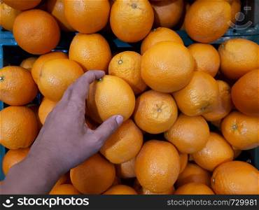Close hand holding orange on stall in supermarket